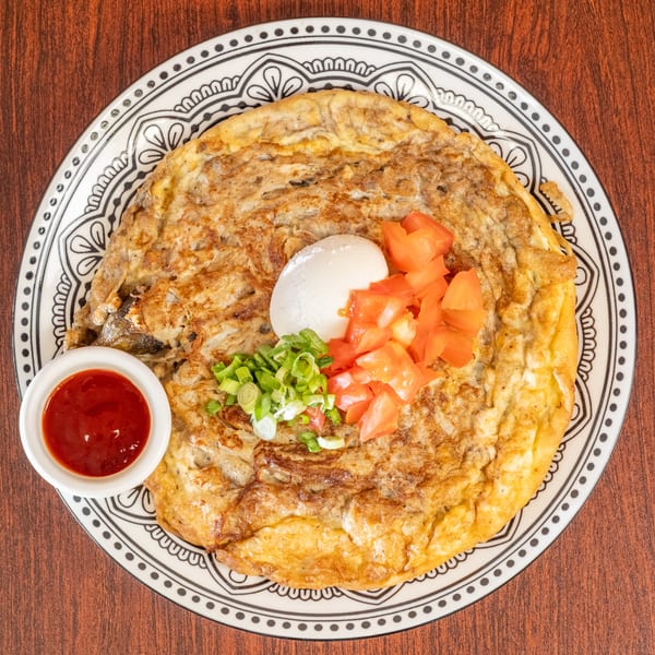 An omelet with chopped tomatoes, green onions, a hard-boiled egg, and a side of chili sauce.