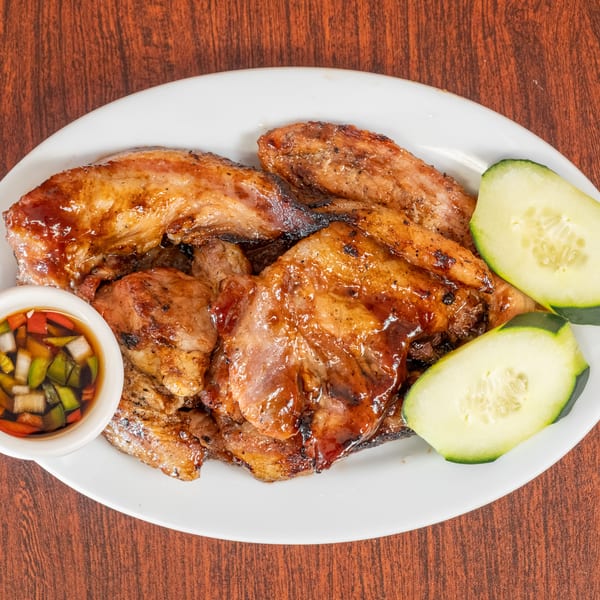 Grilled chicken pieces with a side of cucumber slices and a dipping sauce on a white plate.