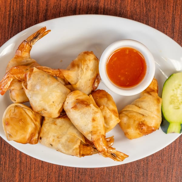 Golden fried shrimp spring rolls with sweet chili sauce and a cucumber slice on a white plate.