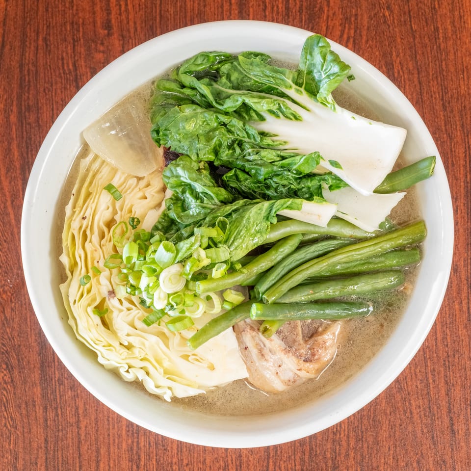 A bowl of Filipino nilaga soup with beef, cabbage, bok choy, green beans, and scallions.