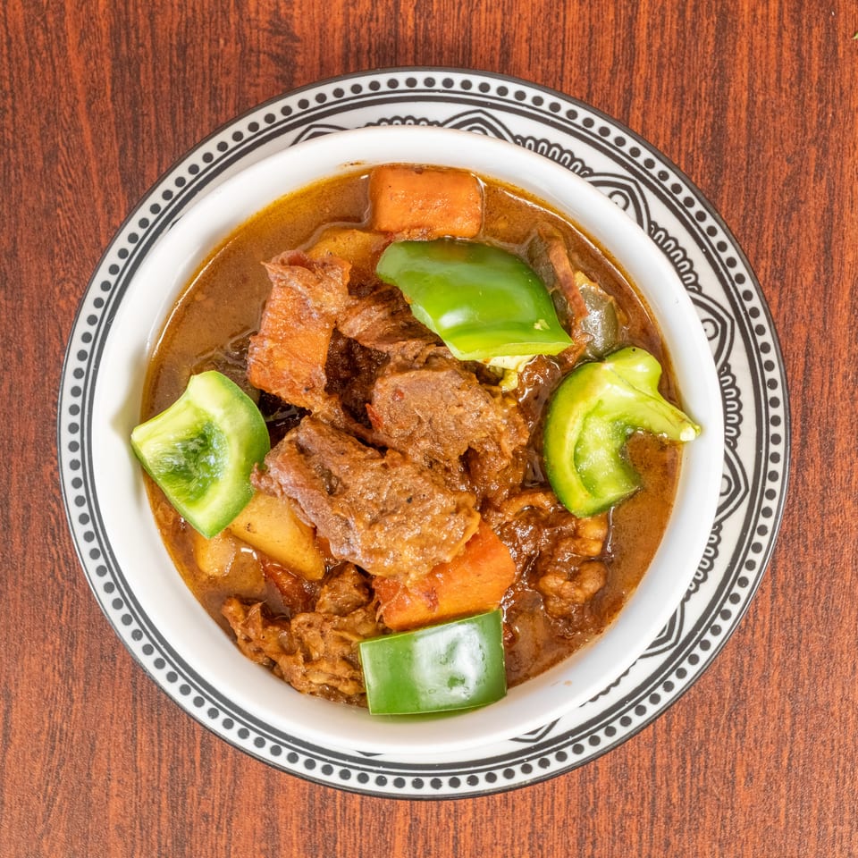 Hearty beef stew with carrots, potatoes, and green bell peppers in a decorative bowl.