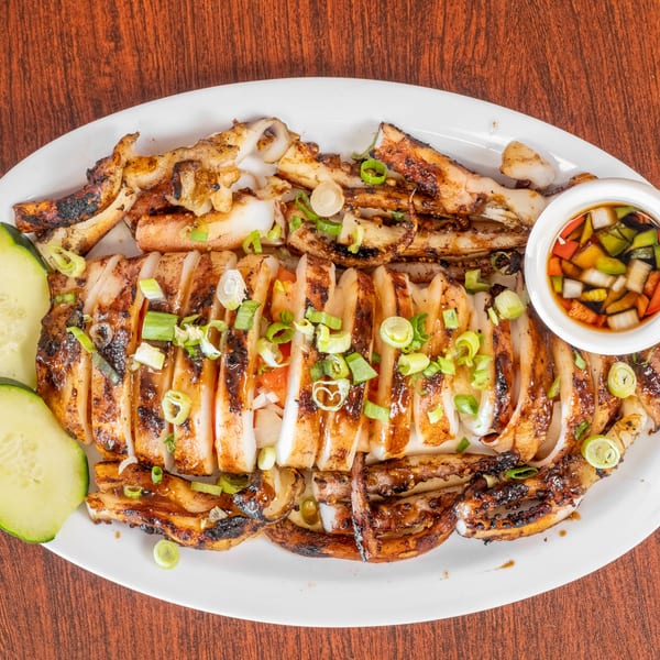 Grilled squid, sliced and garnished with scallions, served with cucumber slices and a dipping sauce.