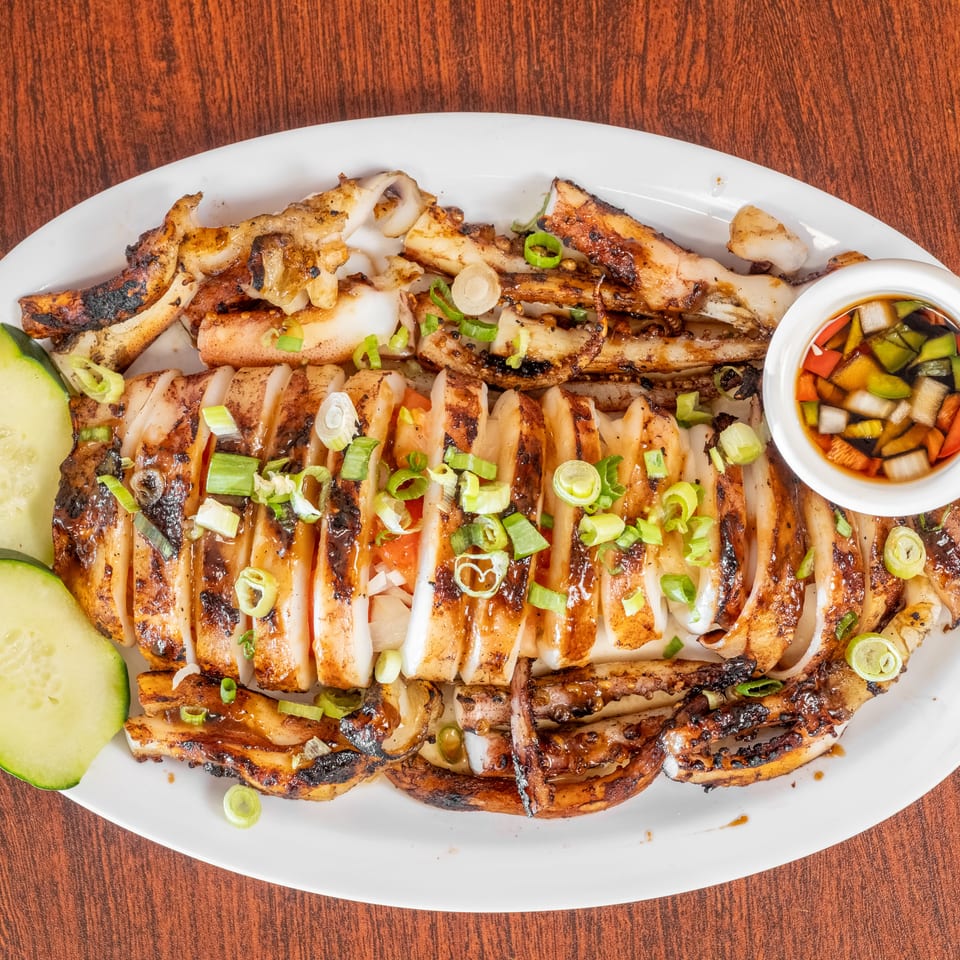 Grilled squid, sliced and garnished with scallions, served with cucumber slices and a dipping sauce.