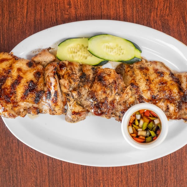 Grilled chicken skewers with cucumber slices and a side of dipping sauce on a white plate.